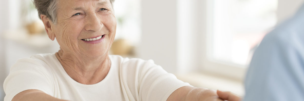 Lächelnde ältere Frau führt mit Theraband Kräftigungsübung durch um fit zu werden und zu bleiben.